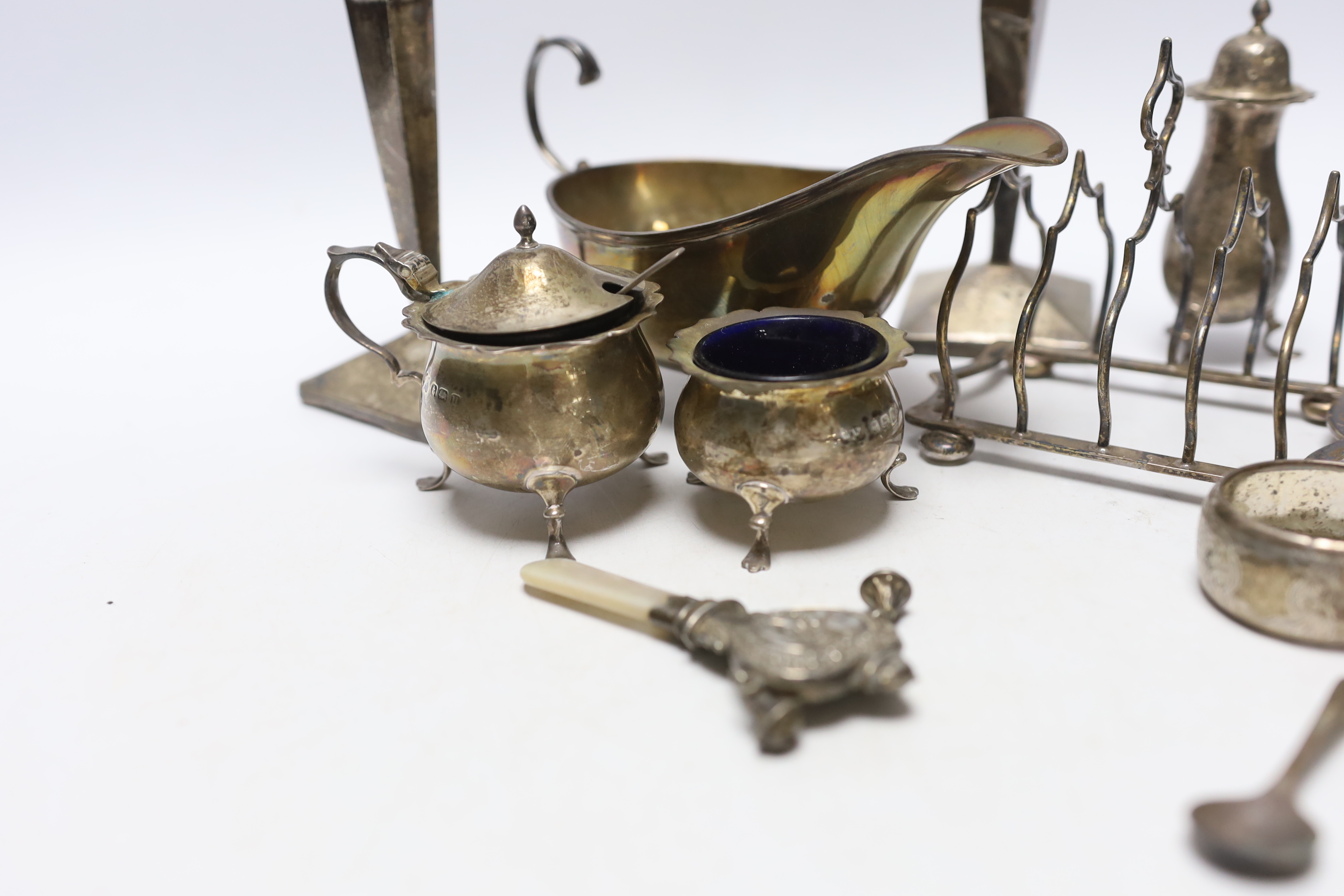 Sundry small silver including an Edwardian silver sauceboat, Birmingham, 1906, pair of spill vases (a.f.), a five bar toastrack, three condiments, a purse, two napkin rings and a child's rattle.